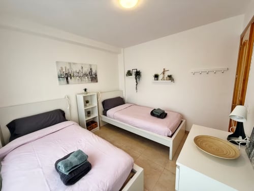 Luminoso apartamento con dormitorio doble en propiedad de playa en Fuengirola, paredes blancas, ropa de cama rosa y mobiliario moderno
