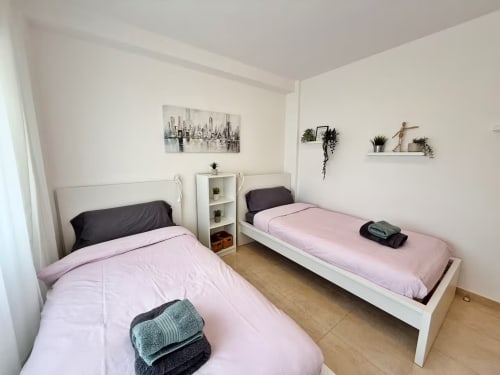 Dormitorio doble con ropa de cama rosa en luminoso apartamento de Fuengirola, muebles blancos, plantas decorativas y cuadros de vistas a la ciudad