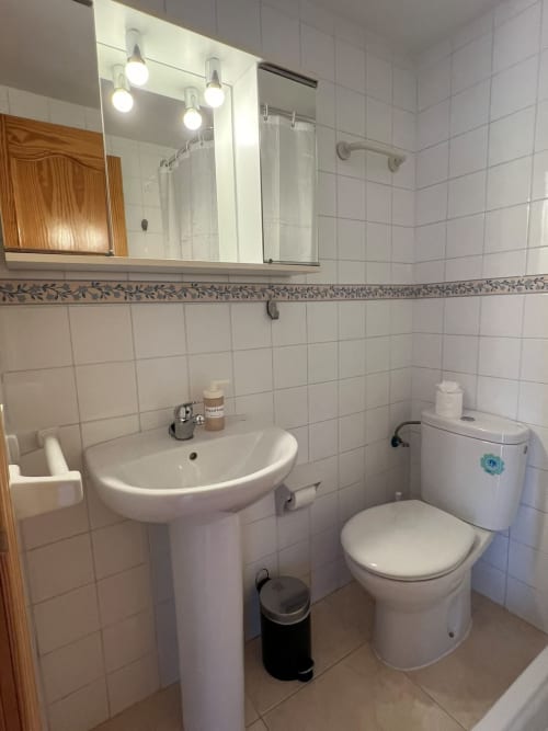 Baño moderno con lavabo de pedestal, inodoro y espejo iluminado en apartamento de playa en Fuengirola