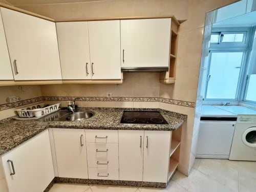 Cocina moderna con armarios blancos, encimera de granito, placa de cocción y fregadero en apartamento frente al mar en Fuengirola