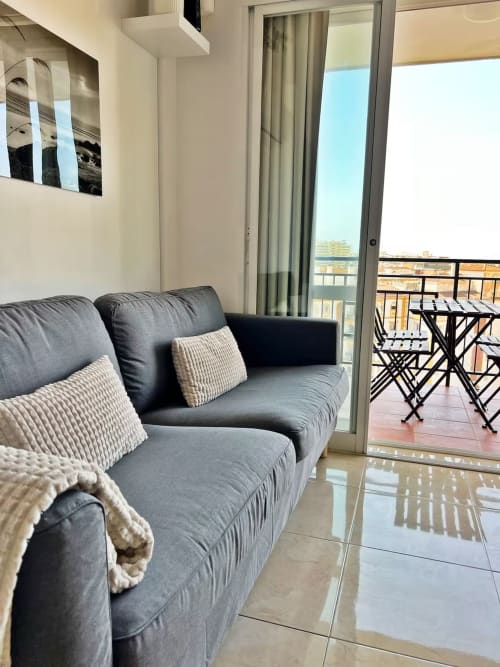 Sofá gris moderno con cojines beige en terraza con vistas a la ciudad de Fuengirola, apartamento de playa con vista al mar