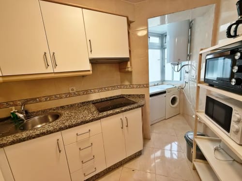 Cocina luminosa en apartamento frente al mar, Fuengirola, con encimeras de granito, armarios color crema y electrodomésticos modernos