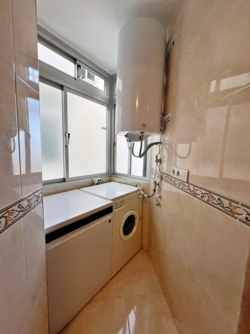 Baño moderno con lavadora, lavamanos y ventana en apartamento de playa en Fuengirola