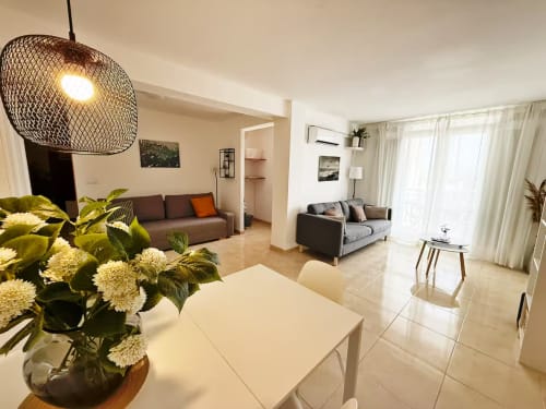 Luminoso salón abierto en apartamento de playa en Fuengirola con mesa de comedor, sofás marrones, lámpara colgante y grandes ventanales