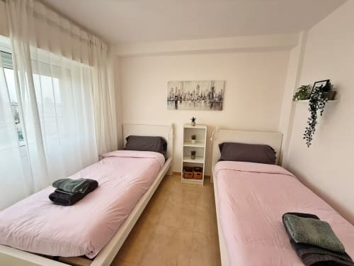 Luminoso dormitorio doble en apartamento de Fuengirola con ropa de cama rosa, cuadros de vistas urbanas, plantas en maceta y comodidades modernas