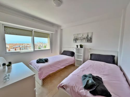 Luminoso dormitorio doble en apartamento de Fuengirola con vistas a la ciudad, ropa de cama rosa y mobiliario moderno