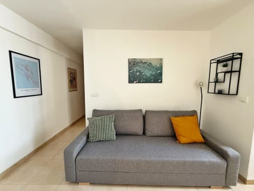 Sofá gris con cojines decorativos en sala de estar de apartamento moderno en Fuengirola con cuadros en las paredes