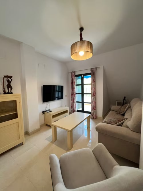 Sala de estar de moderno apartamento en la playa de Fuengirola con asientos beige, muebles de madera y vistas a la ciudad