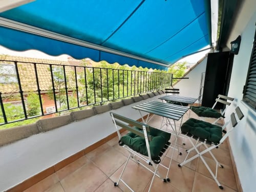 Terraza soleada de apartamento frente al mar en Fuengirola con toldo azul, tumbonas y vistas a la ciudad