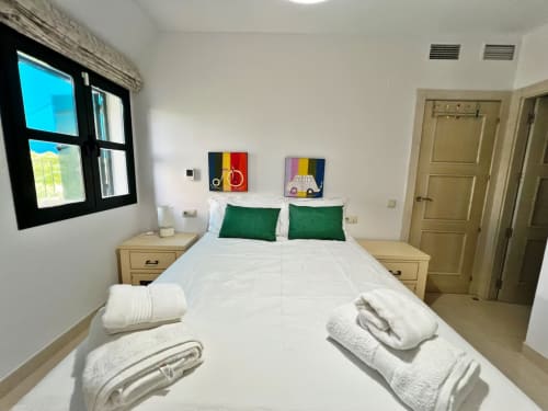 Dormitorio moderno en apartamento frente al mar en Fuengirola con almohadas verdes, muebles de madera y obras de arte coloridas
