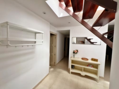 Moderno ático frente al mar en Fuengirola con escalera de madera, paredes blancas y entrada luminosa