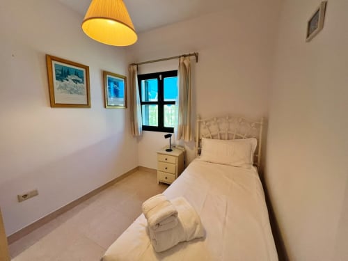 Luminoso dormitorio en apartamento de playa en Fuengirola con cama individual, vistas por ventana, cuadros decorativos y lámpara colgante amarilla