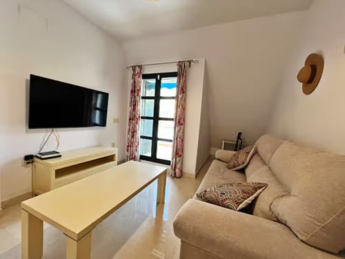 Sala de estar de apartamento moderno frente al mar en Fuengirola con TV, sofá beige, muebles de madera y vista al mar