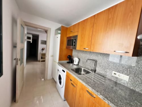 Cocina moderna en apartamento frente al mar, Fuengirola. Muebles de madera, encimera de granito, fregadero de acero inoxidable, lavadora.