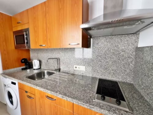 Cocina moderna con muebles naranjas, encimera de granito, fregadero y vitrocerámica de acero inoxidable en apartamento de Fuengirola