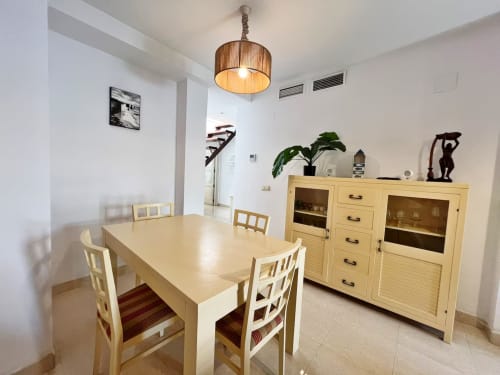 Comedor moderno en apartamento de playa en Fuengirola con mesa de madera, sillas y armario amarillo bajo luz colgante