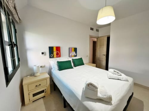 Moderno dormitorio en apartamento frente al mar de Fuengirola con cama queen, almohadas verdes, luz colgante y vistas a la ciudad