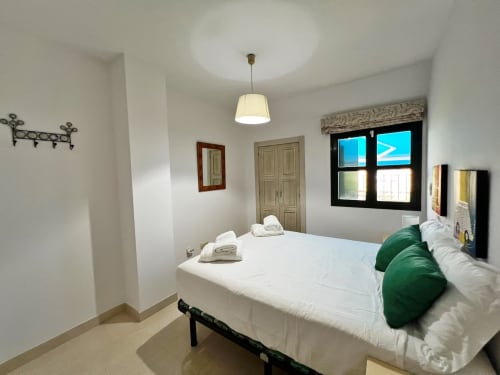 Moderno dormitorio de apartamento frente al mar en Fuengirola con cama queen, cojines verdes, lámpara colgante y vistas a la ciudad