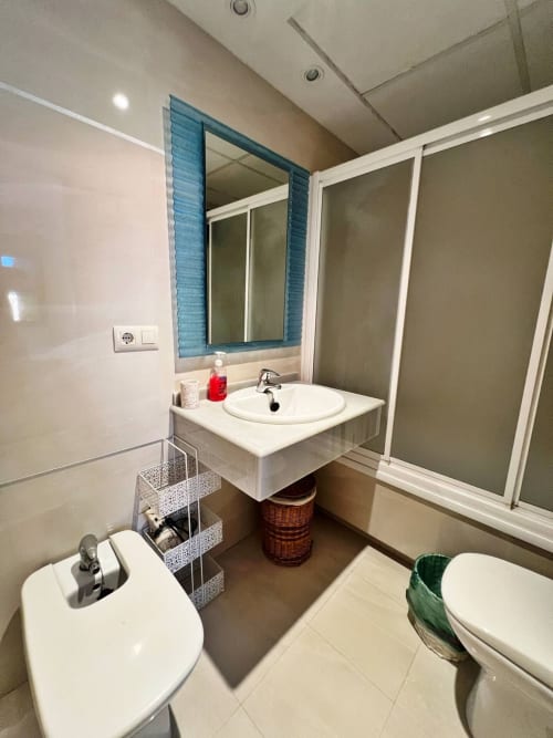 Baño moderno en apartamento de playa en Fuengirola con lavabo blanco, espejo con marco azul, inodoro y piso de cerámica