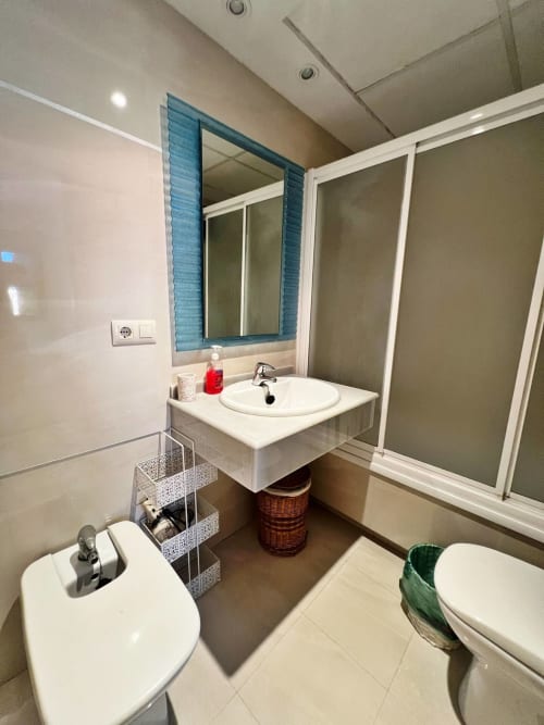 Baño moderno en apartamento de playa en Fuengirola con lavabo, espejo, inodoro y suelo de baldosas blancas