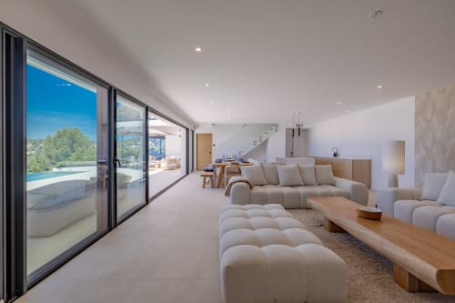 Spacieux séjour ouvert à la villa PERLE D'AZUR avec canapé beige, cuisine moderne, escalier et terrasse vue piscine