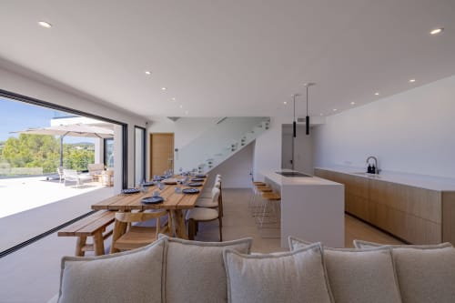 Salle à manger de villa moderne avec vue mer, table en bois, cuisine ouverte et accès à la terrasse à Villa Prestige Azur Antilles