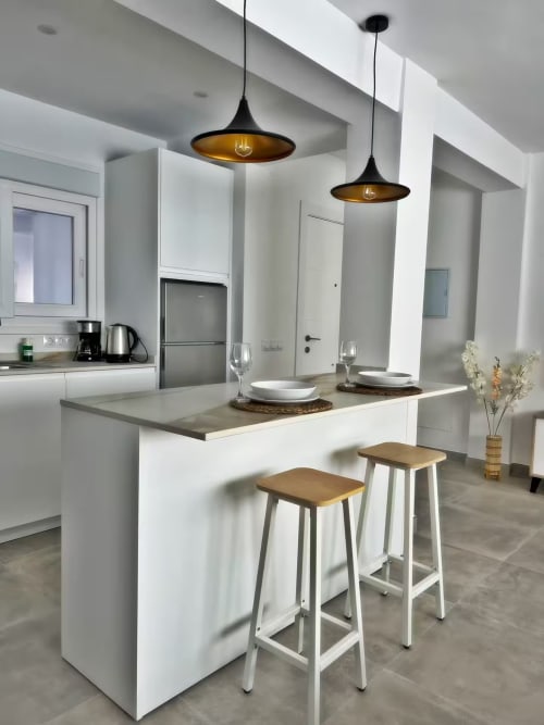 Cocina de apartamento de lujo moderno en Fuengirola con isla blanca, lámparas colgantes, barra y acero inoxidable