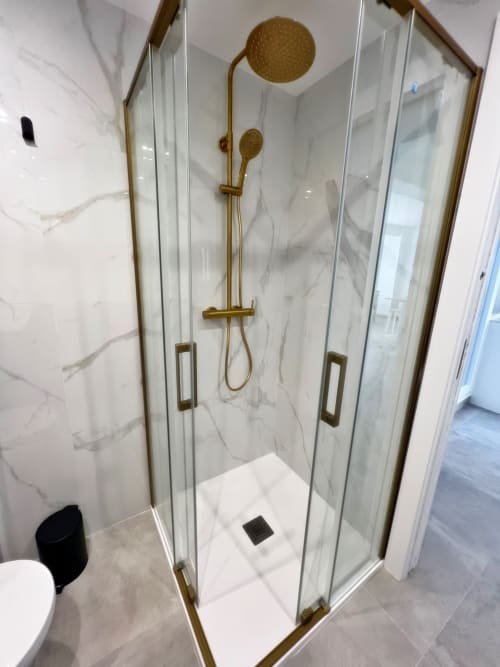 Moderno baño de lujo con paredes de mármol, accesorios dorados y ducha de lluvia en apartamento de Fuengirola