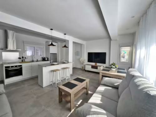 Lujoso apartamento de playa en Fuengirola con salón abierto, cocina blanca moderna, sofá gris, mesas de madera y