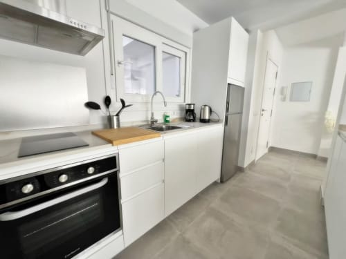 Cocina moderna blanca en apartamento de lujo junto a la playa, Fuengirola. Electrodomésticos de acero inoxidable, encimera de madera, vistas a la ciudad.