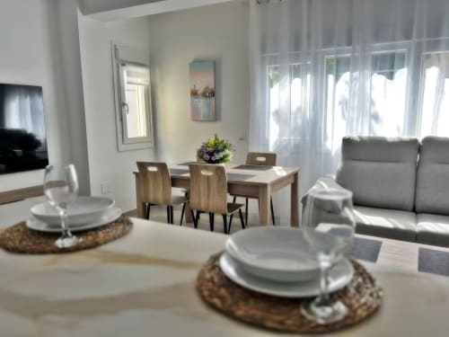 Apartamento de lujo frente al mar en Fuengirola con mesa de comedor moderna, sofá gris y vistas despejadas de la ciudad a través de grandes ventanales
