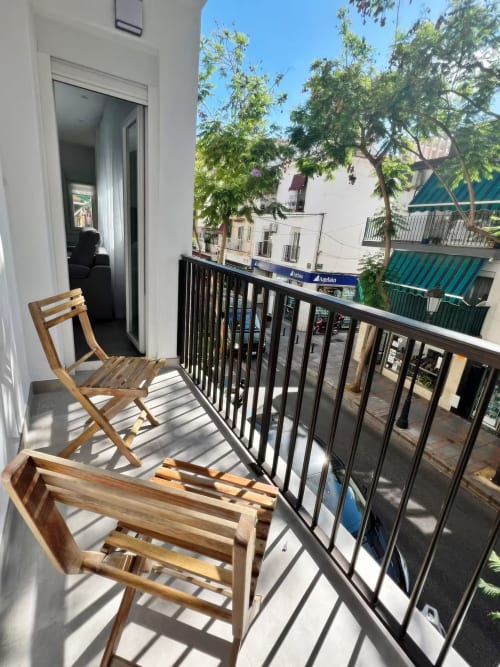 Soleado balcón con sillas de madera con vistas a la calle de Fuengirola, árboles y tiendas en Grupo Inmo House, lujo junto al mar