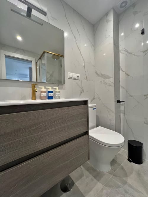 Baño de lujo moderno en apartamento de playa en Fuengirola con paredes de mármol, tocador de madera oscura y ducha tipo lluvia