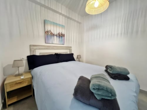 Dormitorio moderno de apartamento de lujo en la playa de Fuengirola con ropa de cama blanca, almohadas negras, toallas dobladas y obra de arte con vista a la ciudad