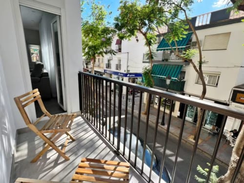 Balcón soleado con silla de madera con vistas a la calle y edificios de Fuengirola en apartamento de lujo
