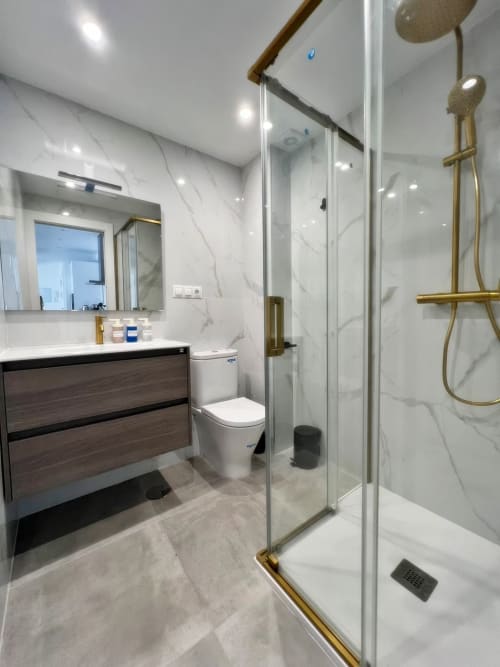 Baño de lujo moderno en apartamento de playa en Fuengirola con paredes de mármol, tocador de madera y ducha de cristal con herrajes de latón