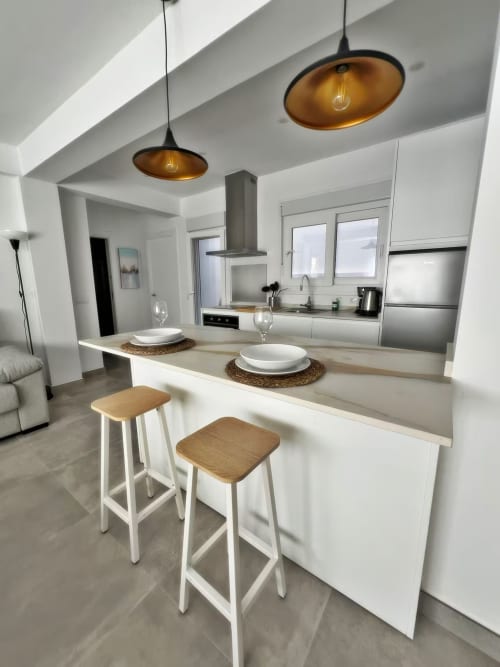 Cocina de lujo moderno en apartamento de playa en Fuengirola con isla blanca, taburetes de madera y lámparas colgantes doradas