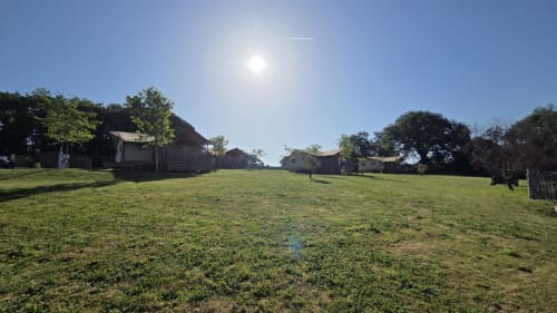 Glamping-terrein van Home Sweet Lodge in Aquitanië met rustieke hutten, groen gazon en bomen onder blauwe hemel