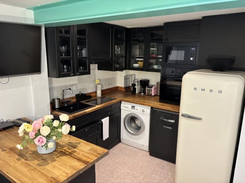 Modern Parisian duplex kitchen with black cabinetry, cream SMEG fridge, wooden counters, and fresh flowers at island