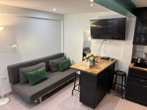 Modern living area in Duplex Marais apartment with gray sofa, green pillows, wooden counter, and wall-mounted TV in Paris