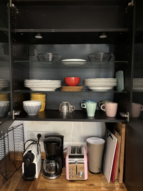 Modern kitchen cabinet display with dishware, mugs, and appliances in Paris apartment