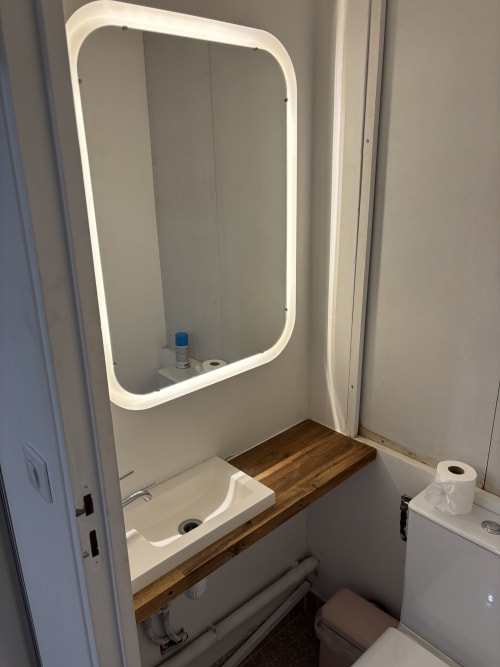 Modern bathroom in Duplex Marais apartment with illuminated mirror, white sink, wooden counter, and toilet at Paris hotel