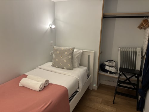 Cozy bedroom in Duplex Marais apartment, Paris with single bed, patterned pillows, rolled towels, and radiator heating