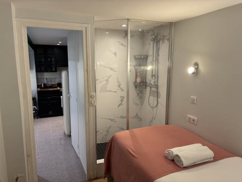 Modern bedroom in Duplex Marais Paris apartment with ensuite shower, terracotta bed, and glass bathroom enclosure