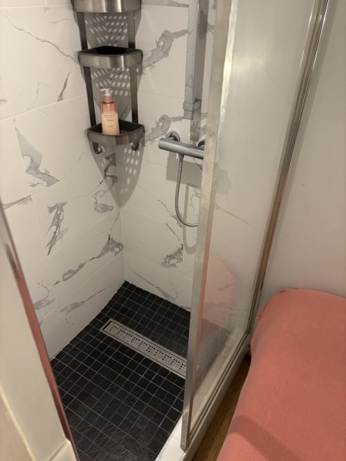 Modern shower in Duplex Marais apartment with marble tiles, stainless steel caddy, and rainfall showerhead at ALDARO Paris.