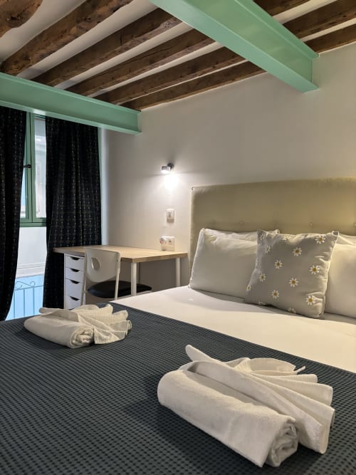 Duplex Marais bedroom with queen bed, desk, exposed beams, green accents, black curtains, rolled towels on bed at Aldaro