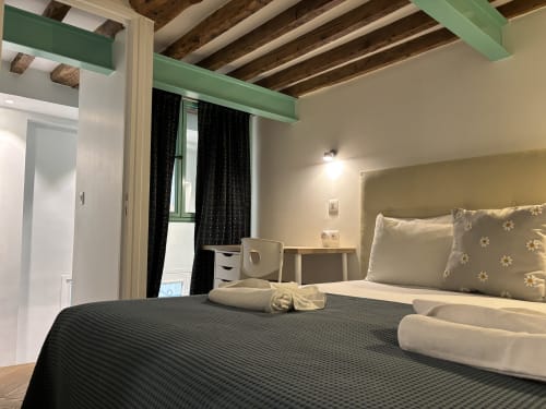 Duplex Marais bedroom in Paris with exposed beams, green accents, black curtains, and comfortable bed