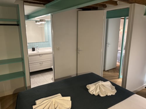 Modern duplex bedroom with ensuite bathroom, turquoise accents, dark bed, and mirrored wardrobe in Paris Marais hotel