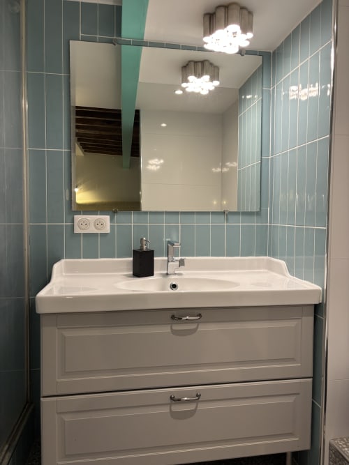 Modern bathroom in Duplex Marais apartment with mint green tile, white sink vanity, mirror, and cloud-shaped ceiling lights