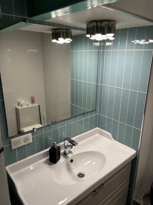 Modern bathroom in Paris Duplex Marais apartment with white sink, chrome faucet, teal tile walls, and contemporary lighting